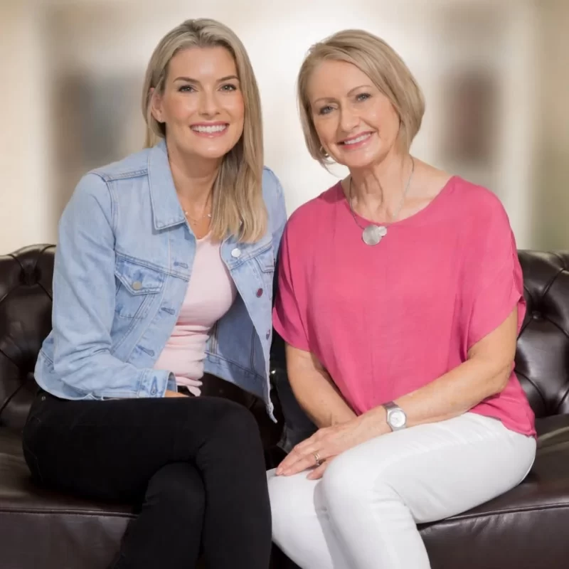 Two women smiling together on a leather couch