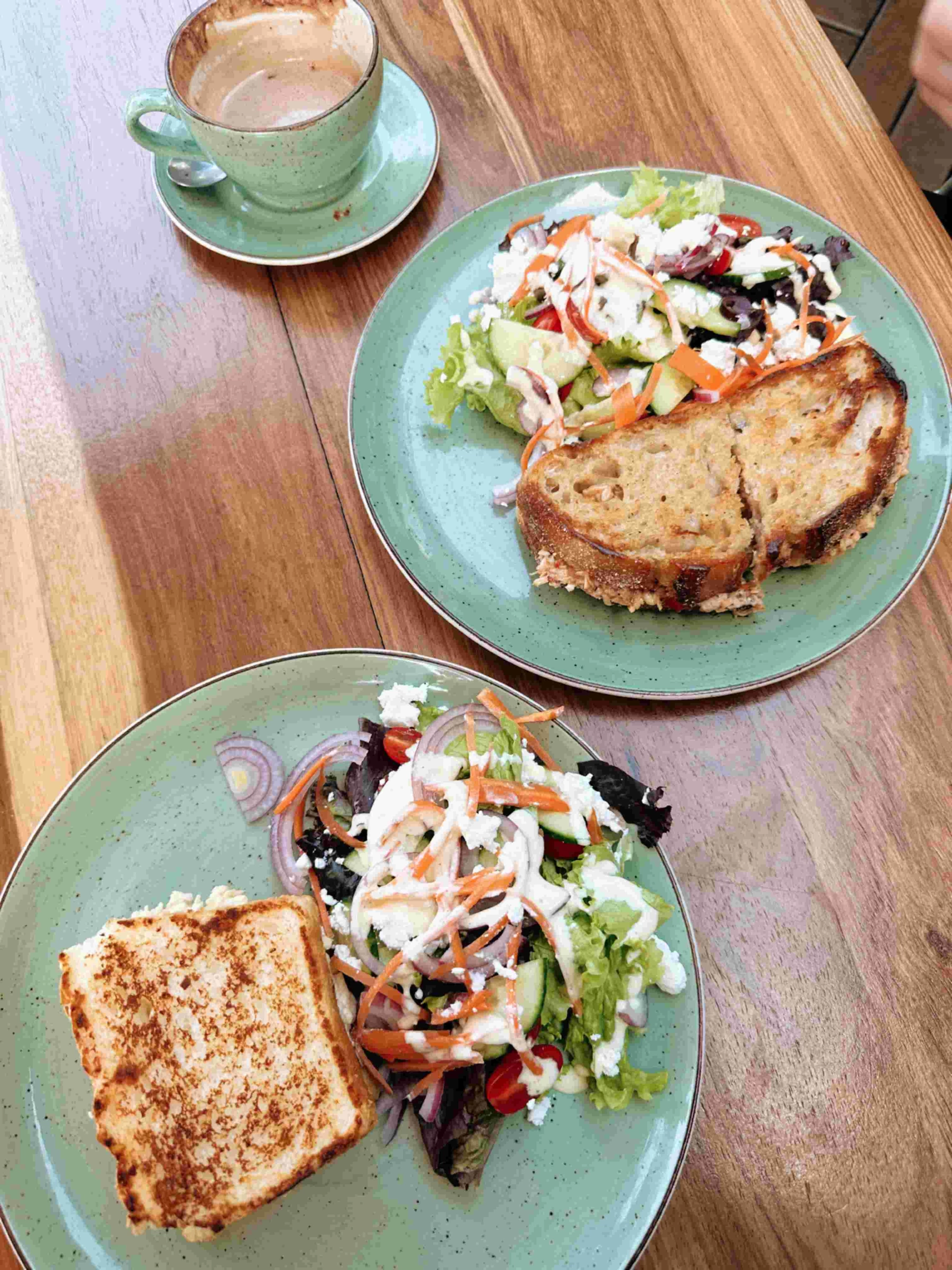 Two plates of toasted sandwiches with fresh salads and coffee