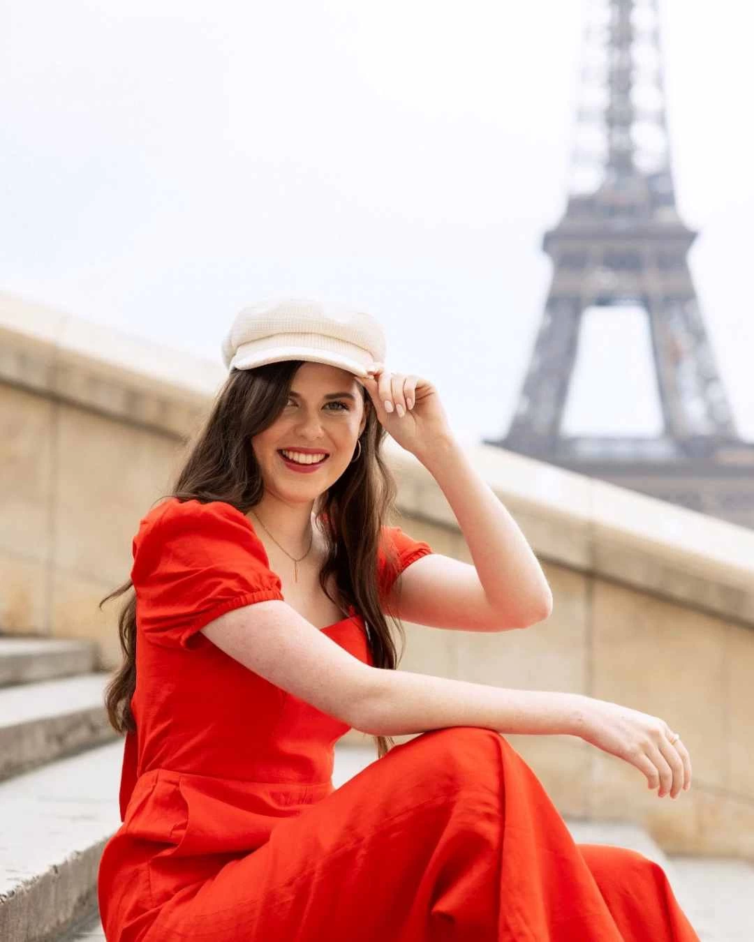 Woman in red dress and white cap posing near Eiffel Tower