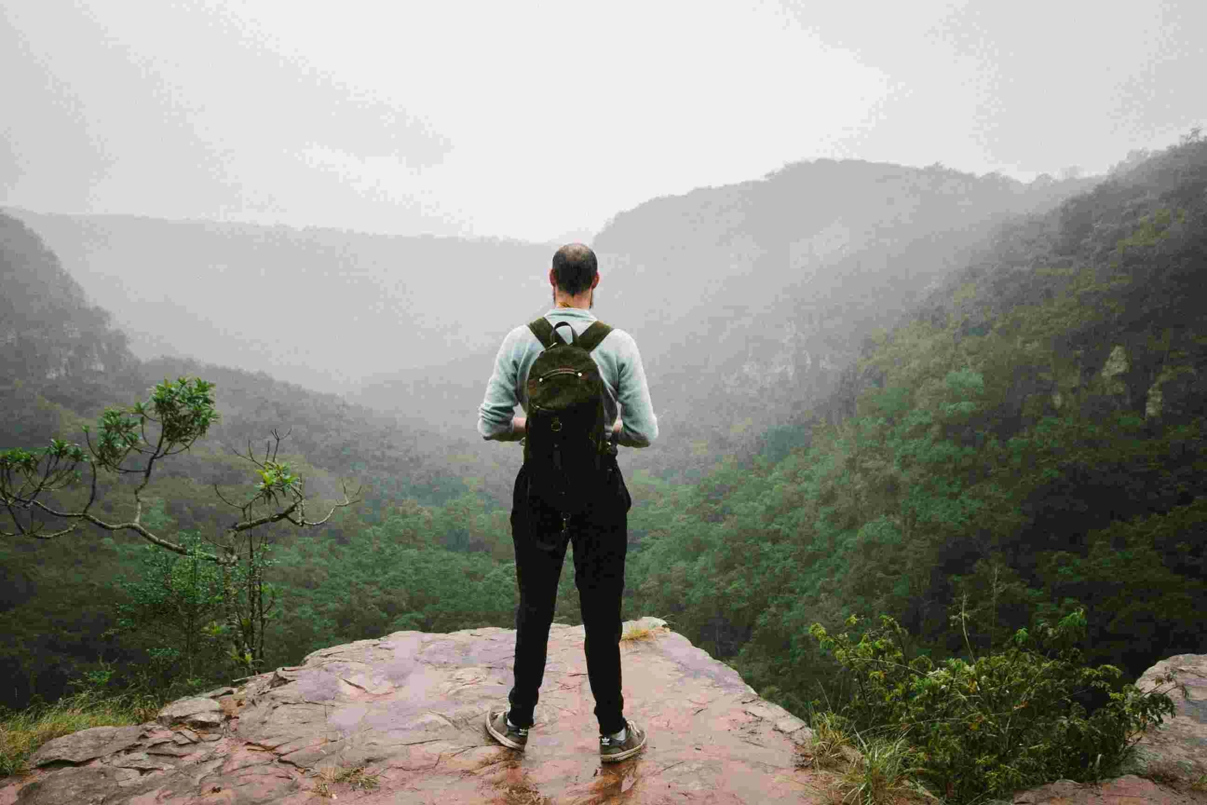 Hiker with backpack overlooking misty green gorge