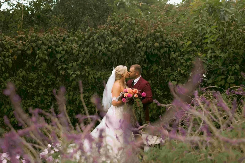 Bride and groom kissing among purple wildflowers in a garden