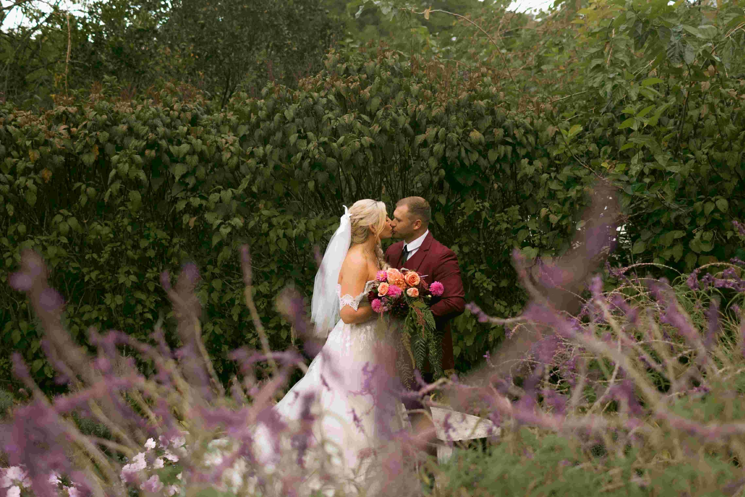 Bride and groom kissing among purple wildflowers in a garden
