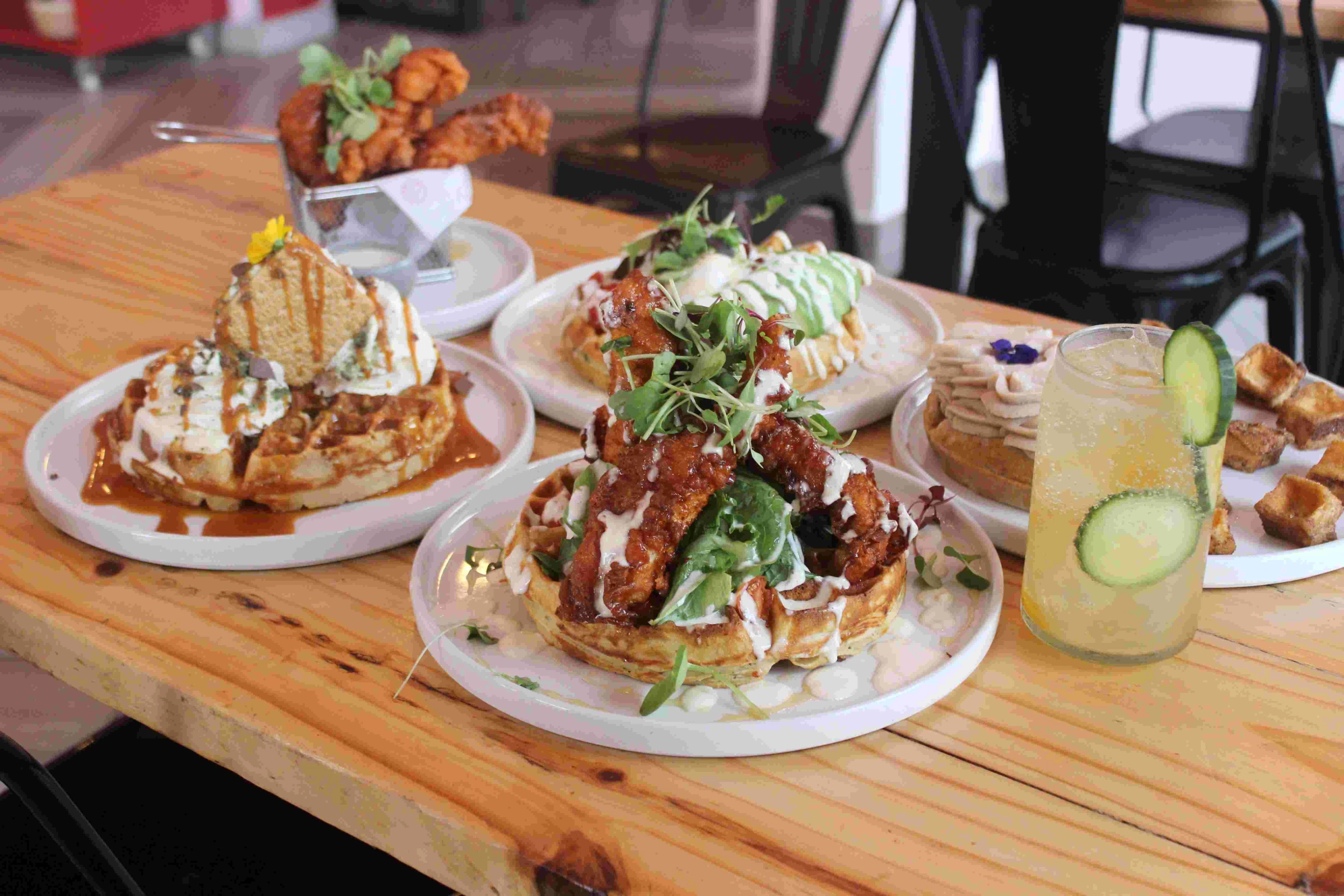 Loaded chicken and waffle dishes with a cocktail on a table