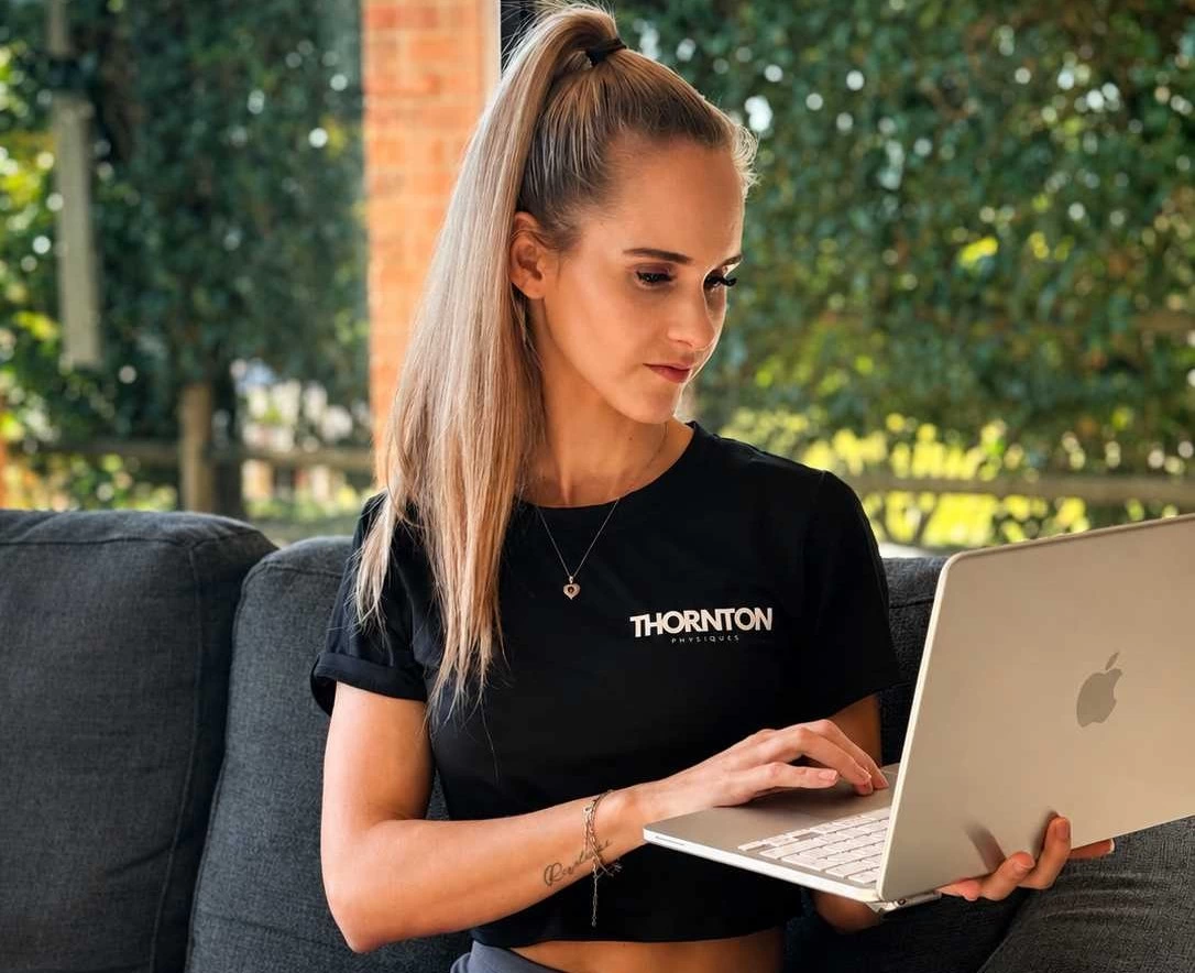 Fitness trainer in black Thornton Physiques shirt on a laptop