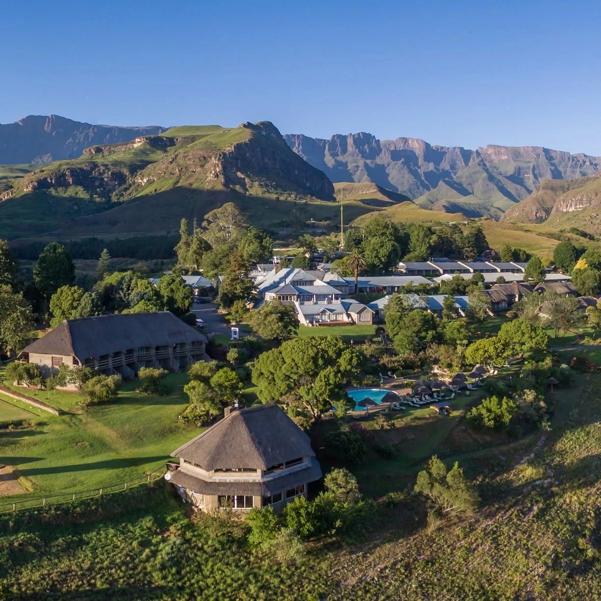 Aerial view of thatched-roof resort beneath Drakensberg mountains